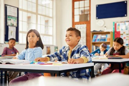 Four children sit at their desks in a classroom with good indoor air quality after a duct cleaning