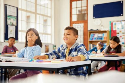 Four children sit at their desks in a classroom with good indoor air quality after a duct cleaning